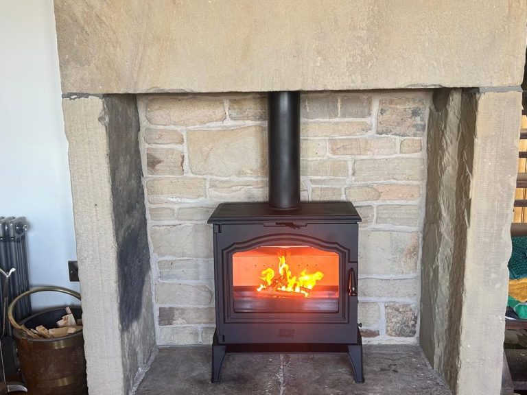 A black wood-burning stove with a glowing fire inside, set against a stone wall.