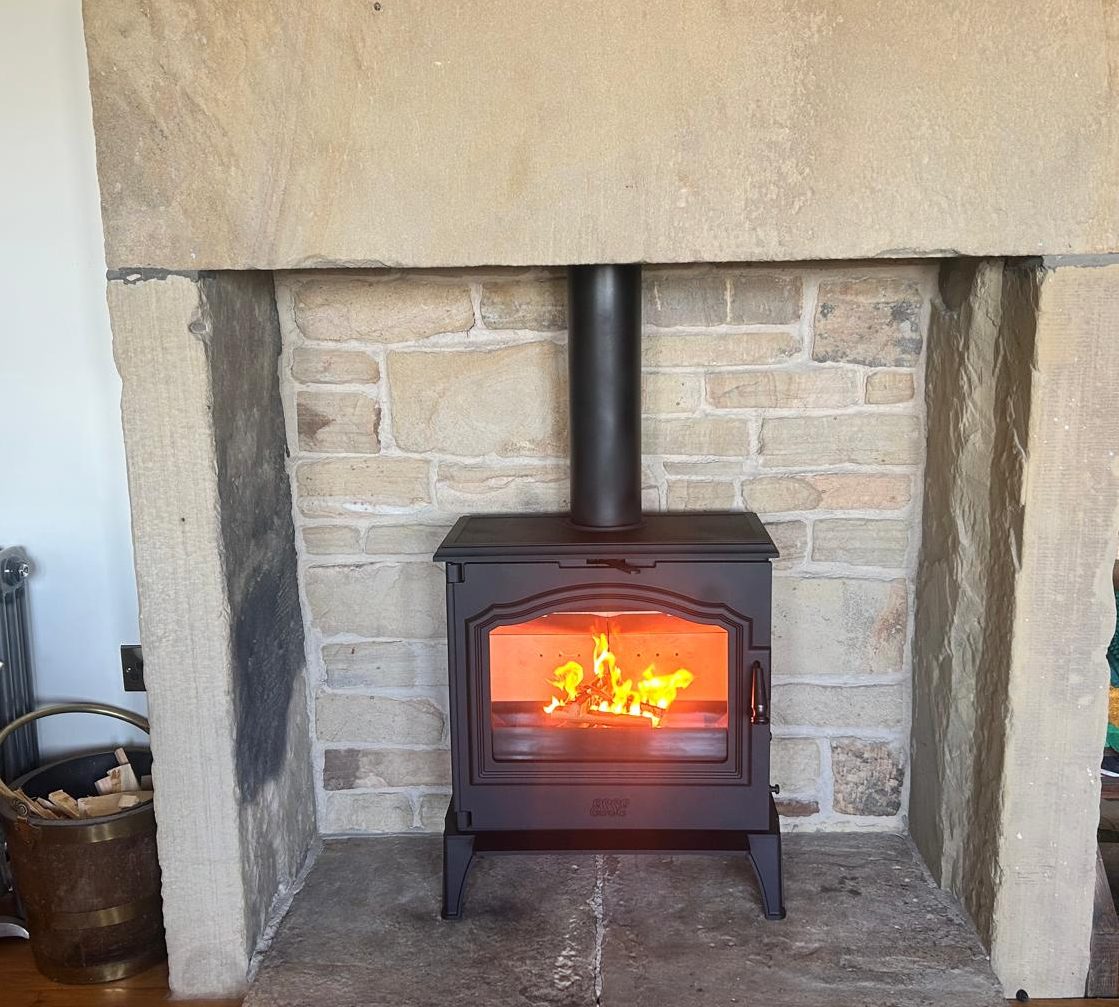 Black wood-burning stove with a glowing fire, nestled in a stone fireplace.