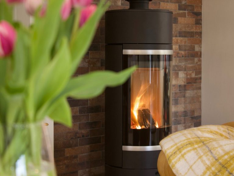 Modern wood burner with flames, set against a rustic stone wall and a flower bouquet nearby.