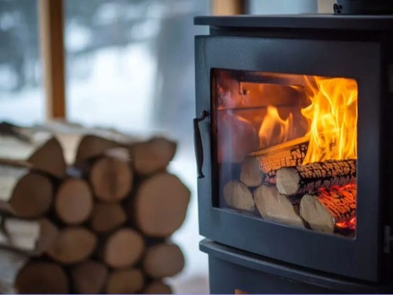 A wood-burning stove with a glowing fire and a stack of logs nearby.